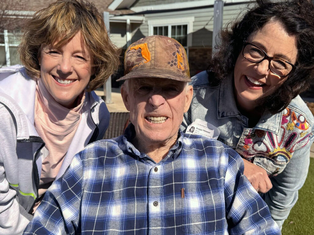 Two volunteers and one resident were smiling for a photo on a green lawn in a senior living neighborhood, showcasing community spirit.