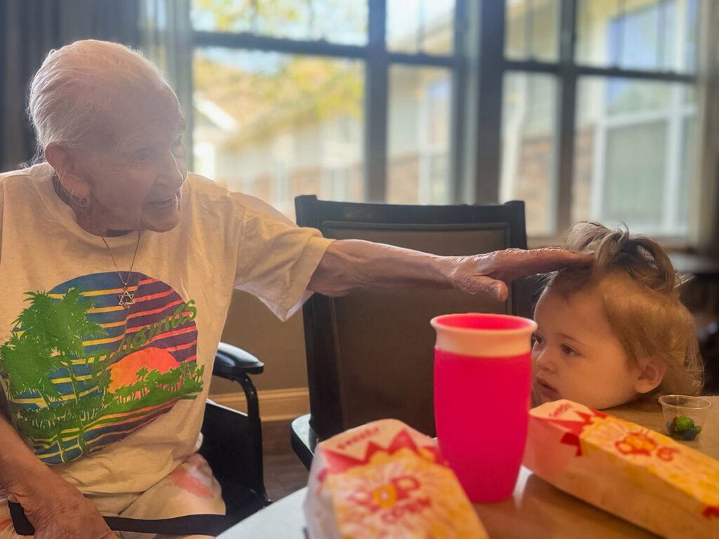 A memory care resident sitting with a small child, both enjoying popcorn as a snack.