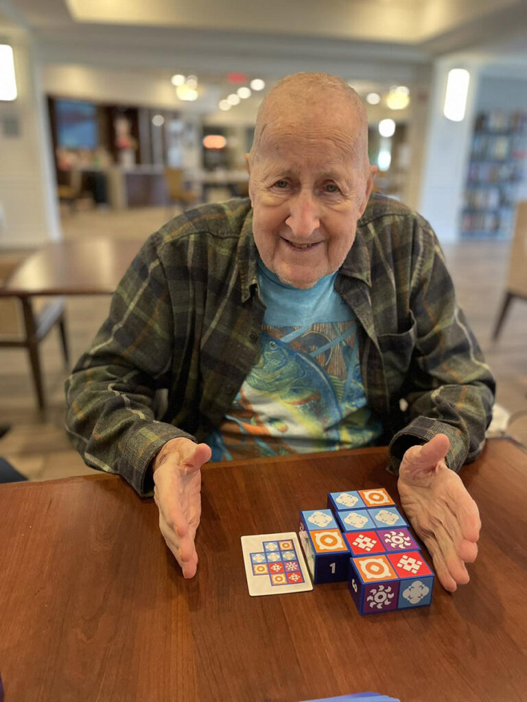 An elderly man proudly displaying his victory in the game of the Uzzle, surrounded by dice at a table.