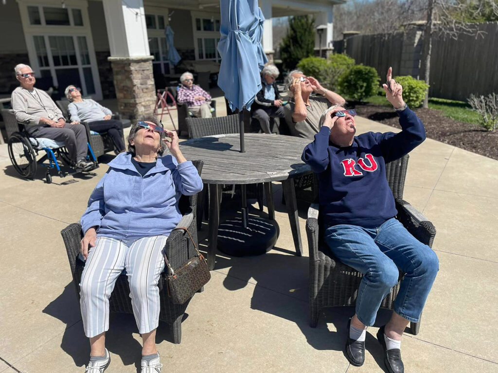 Senior residents sitting with hands up, safely watching a solar eclipse together.