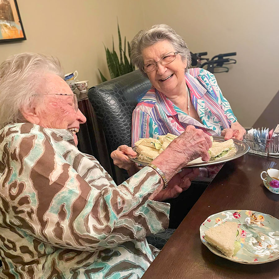 Two elegant senior ladies savoring a delightful lunch at a table, relishing a hosted tea party with cucumber sandwiches.