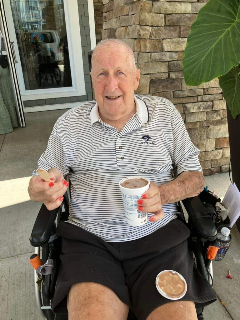 Senior living community resident sitting in a wheelchair, smiling, and enjoying ice cream with red painted nails.